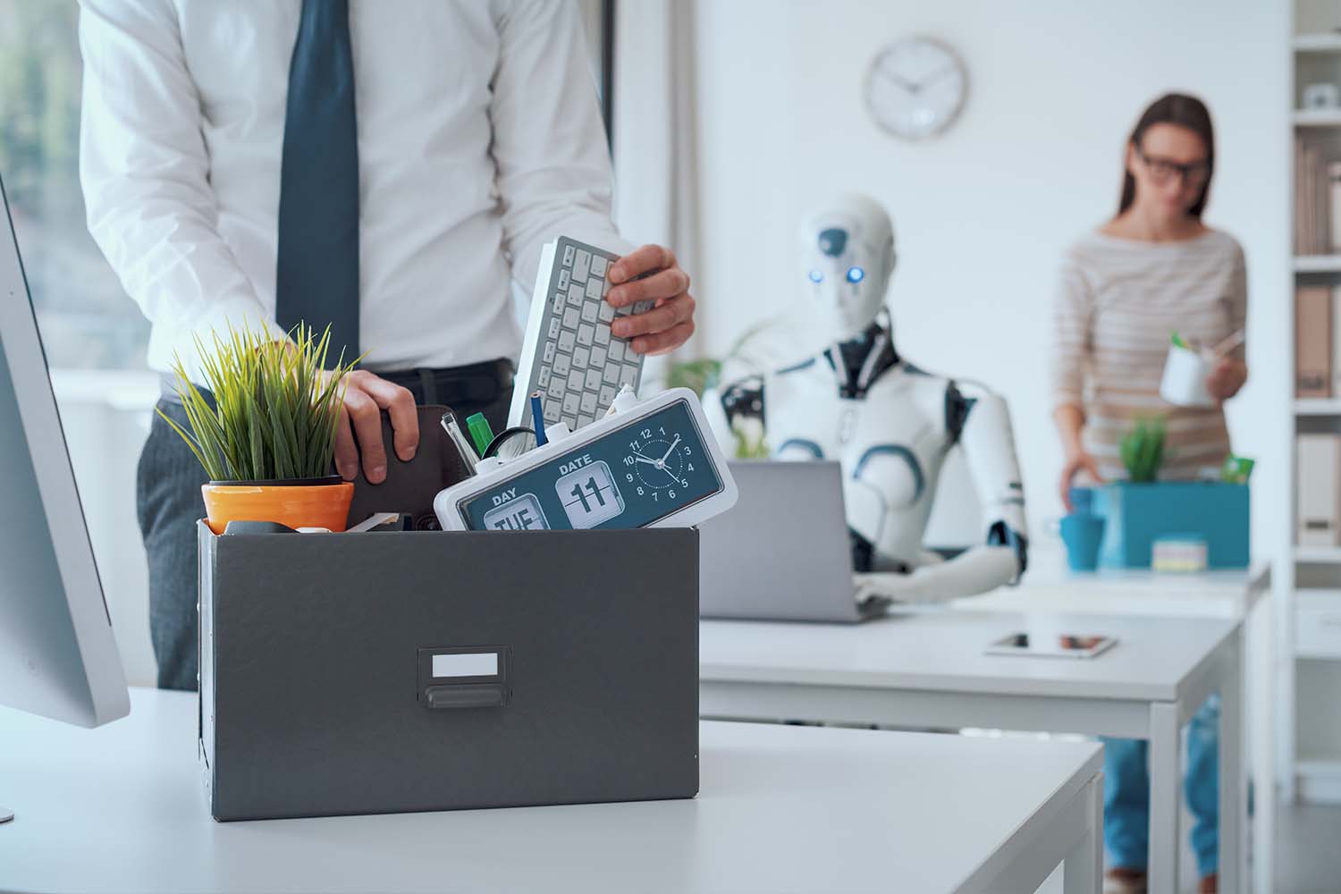 A terminated employee packing an office box while a robot operates in the background, a stark conceptual symbol of corporate ai job loss.