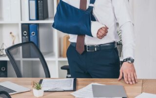 An injured office worker with an arm sling standing at his desk, highlighting the importance of mandatory workers compensation utah insurance.