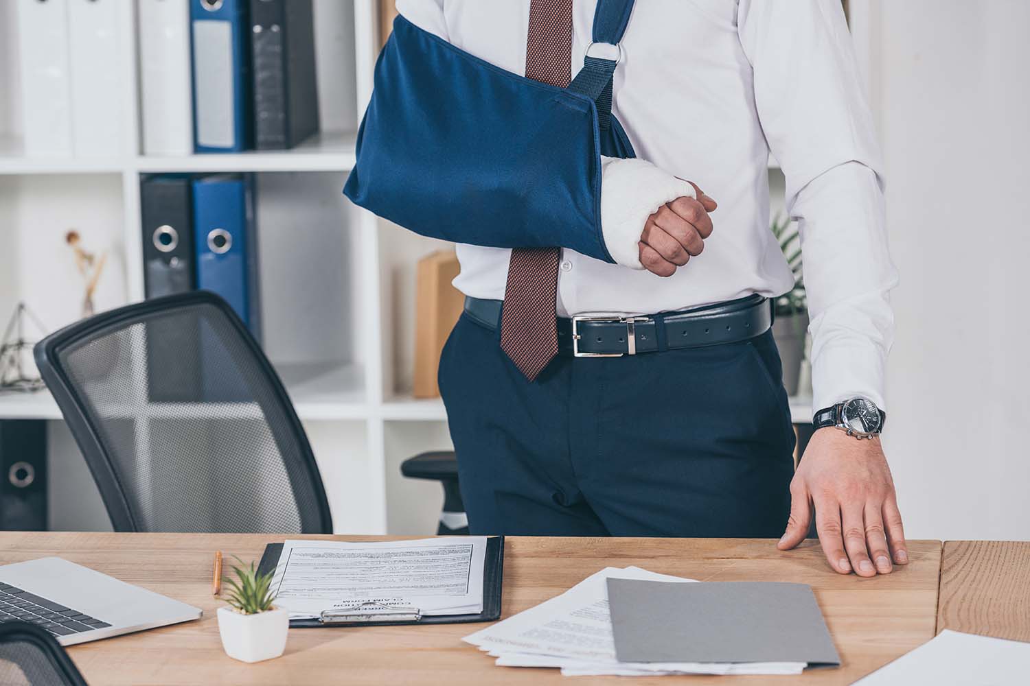 An injured office worker with an arm sling standing at his desk, highlighting the importance of mandatory workers compensation utah insurance.
