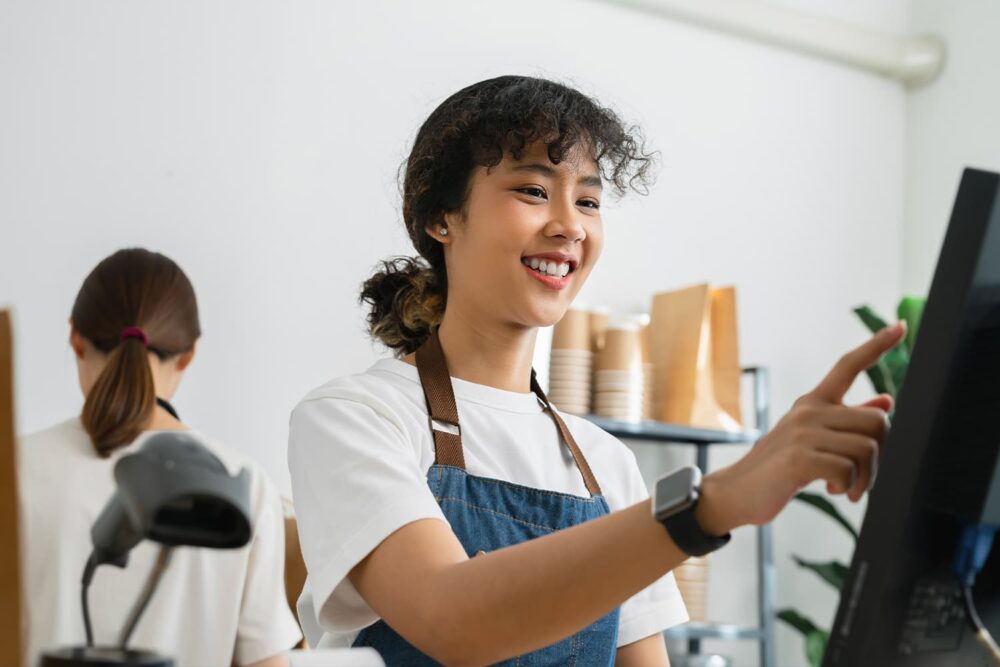 A young cashier smiling while using a point-of-sale system, representing shifts governed by how late can a minor work in utah laws.