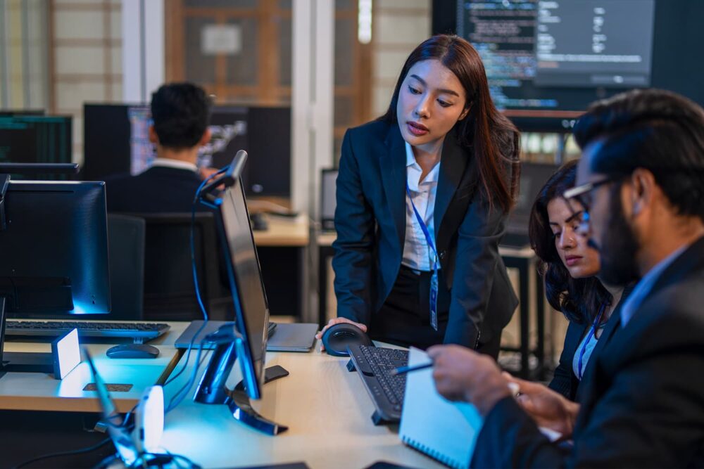 A woman pointing at a computer monitor to guide a colleague, representing operational tech support roles and the changing ai impact on jobs.