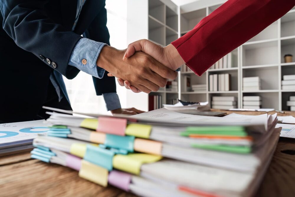 Business partners shaking hands over a stack of legal files. Essential for securing proper workers compensation insurance utah coverage.