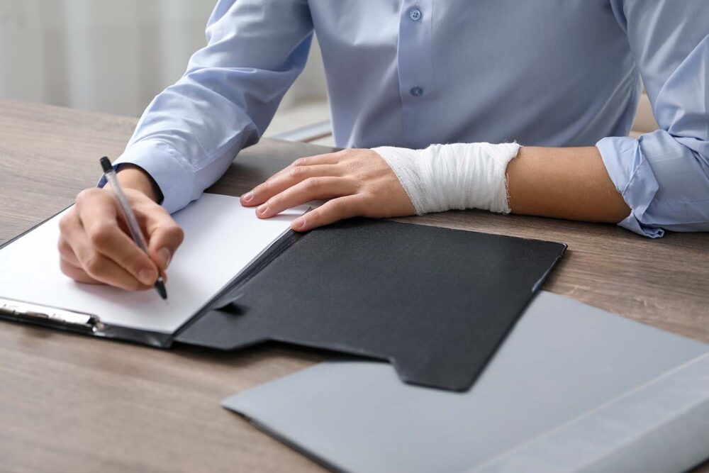A worker with a bandaged wrist filling out legal paperwork. Relevant for businesses reviewing a workers comp waiver utah form.