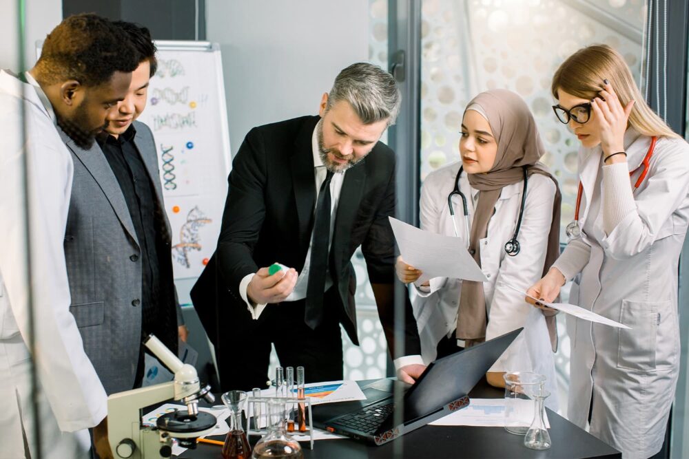 An executive in a suit reviewing data with scientists in a lab, highlighting full-service life science staffing and technical talent matching.