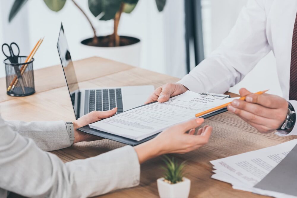Close-up of an employee passing a clipboard claim form to a manager. Demonstrating the process of utilizing utah workers compensation benefits.