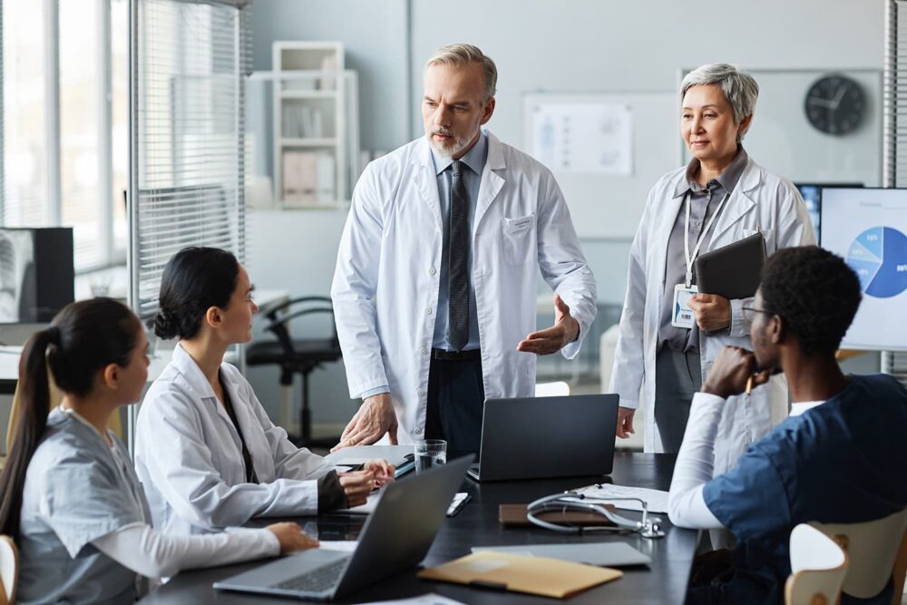 Senior medical leaders in lab coats evaluating team data. Top life sciences executive search firms target candidates with this level of authority.