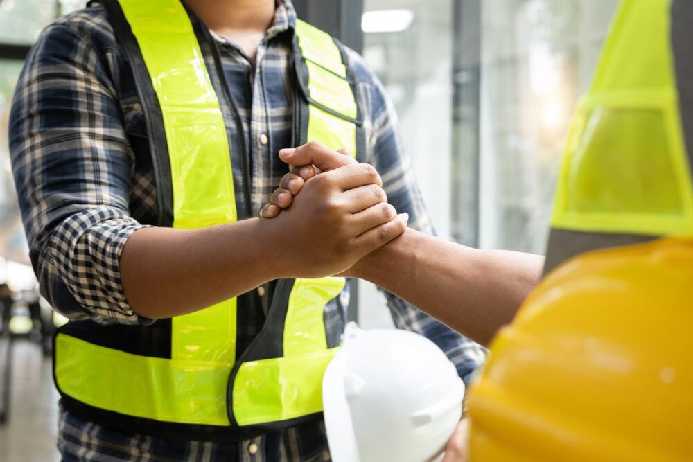 Two workers in high-visibility vests shaking hands, emphasizing industries restricted by strict federal and state minor labor laws.