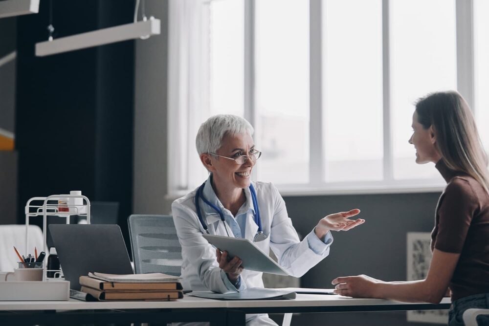 A smiling physician explaining test results on a digital tablet to an injured employee, covered under utah workers comp insurance plans.