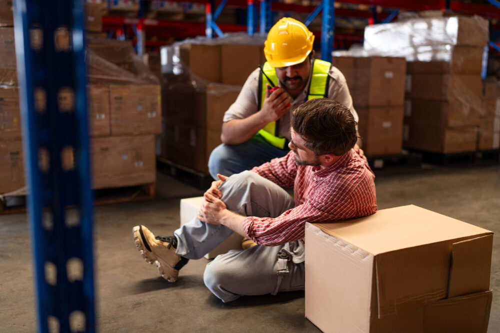 A warehouse worker holding his injured knee while a supervisor uses a walkie-talkie, illustrating a core workers compensation utah incident.