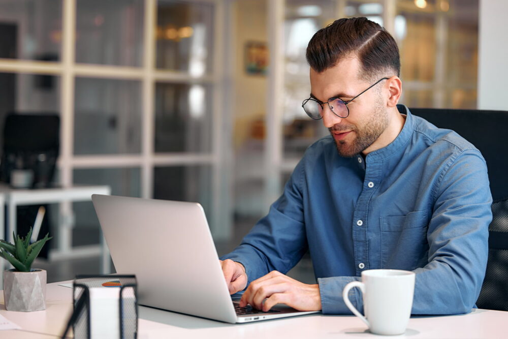 A man smiling while working on his laptop, representing standard white-collar roles frequently analyzed in jobs replaced by ai data.