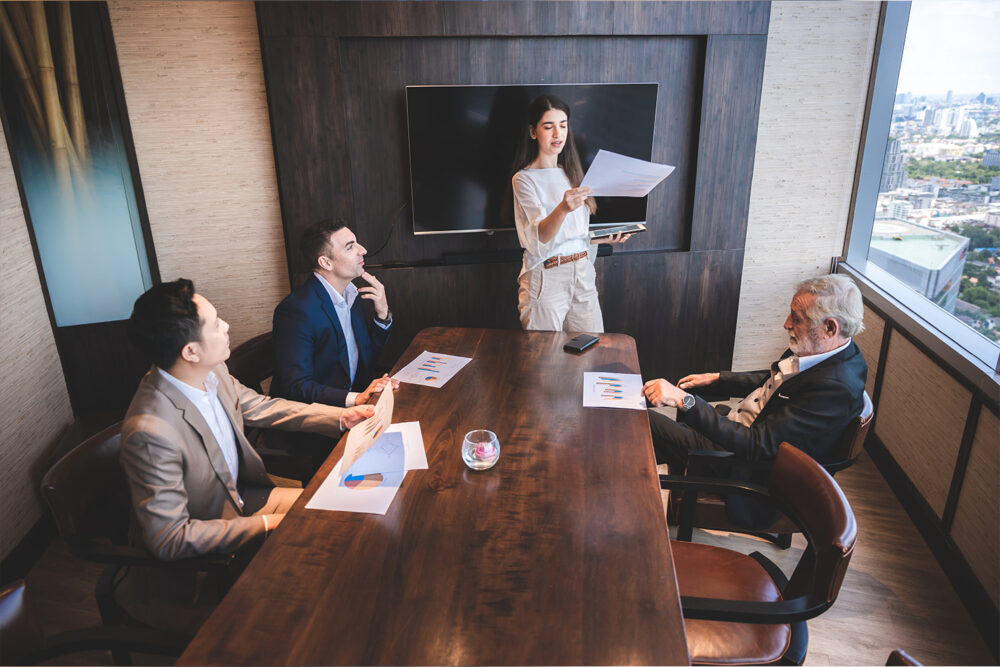 Finance director presenting bar chart financial results to senior executives in a wood paneled boardroom, covering core reporting responsibilities