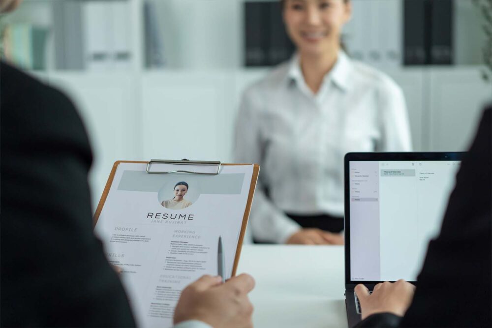 Interviewer reviewing a printed resume on a clipboard beside a laptop, showing where AI in the recruitment process supports screening