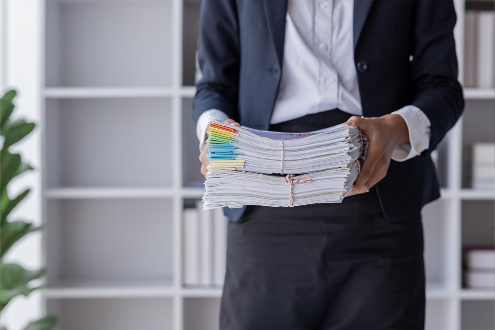 Businesswoman holding thick stacks of paper resumes, highlighting the manual workload that AI recruitment software helps eliminate