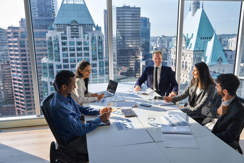 Finance director leading a boardroom meeting with five colleagues reviewing quarterly reports against a floor to ceiling city skyline view