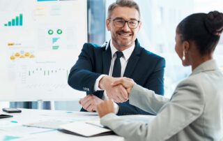 Finance director recruitment handshake between two executives in front of a whiteboard filled with marketing and revenue projection charts